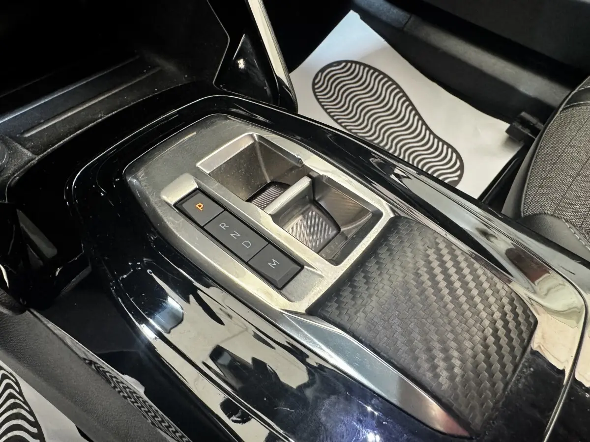 Gros plan sur la console centrale noire brillante du Peugeot 2008 avec sélecteur de boîte automatique et finition carbone.