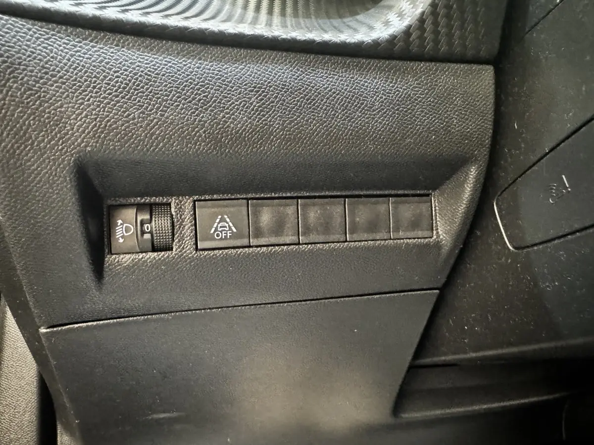 Détail intérieur montrant les commandes de réglage des phares et de désactivation de l'assistance au maintien de voie sur Peugeot 2008 noir.