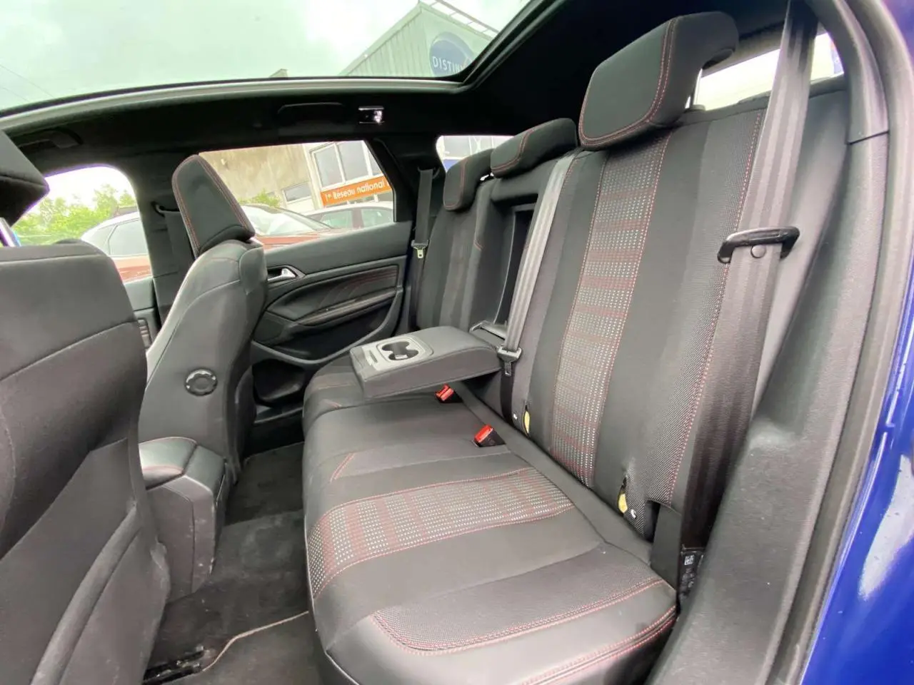 Vue intérieure côté droit des sièges arrière d'une Peugeot 308 SW bleu magnétique avec surpiqûres rouges et toit panoramique.