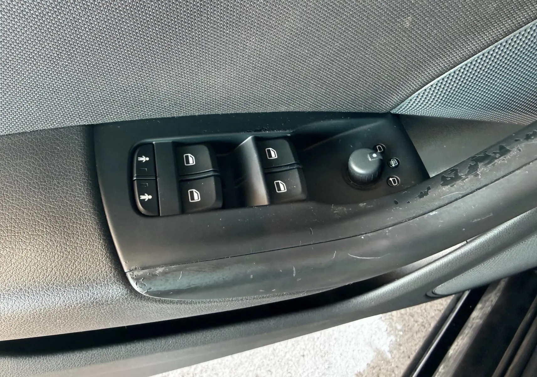 Gros plan sur les commandes de lève-vitres et réglage des rétroviseurs côté conducteur d’un Audi Q3 noir de 2016.