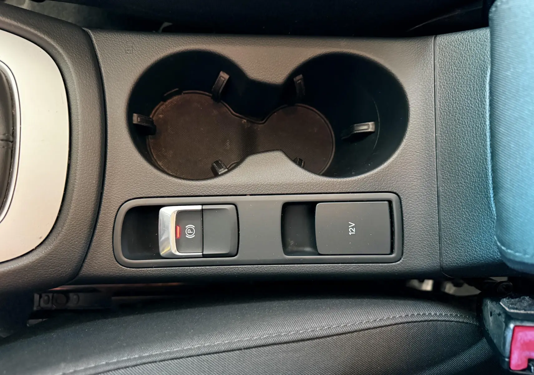 Vue rapprochée de la console centrale noire de l'Audi Q3 2016, avec porte-gobelets et bouton frein à main électrique.