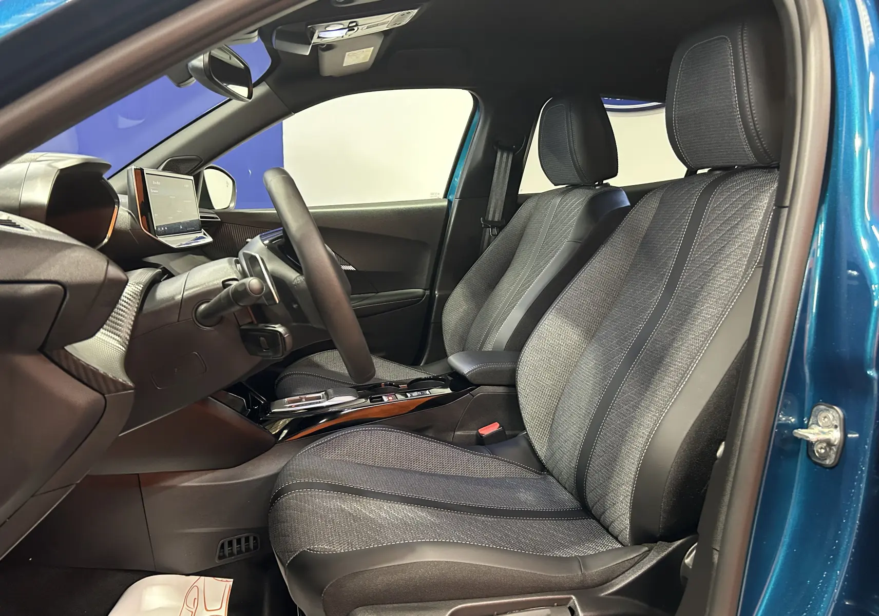 Vue intérieure côté conducteur du Peugeot 2008 bleu Obsession, mettant en valeur les sièges tissu et la planche de bord moderne.