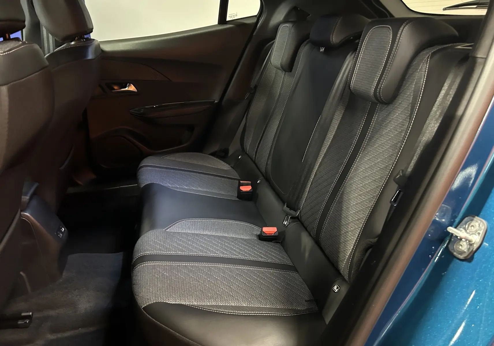 Vue intérieure arrière droite des sièges en tissu et cuir noir du Peugeot 2008 Bleu Obsession 2025, porte ouverte.