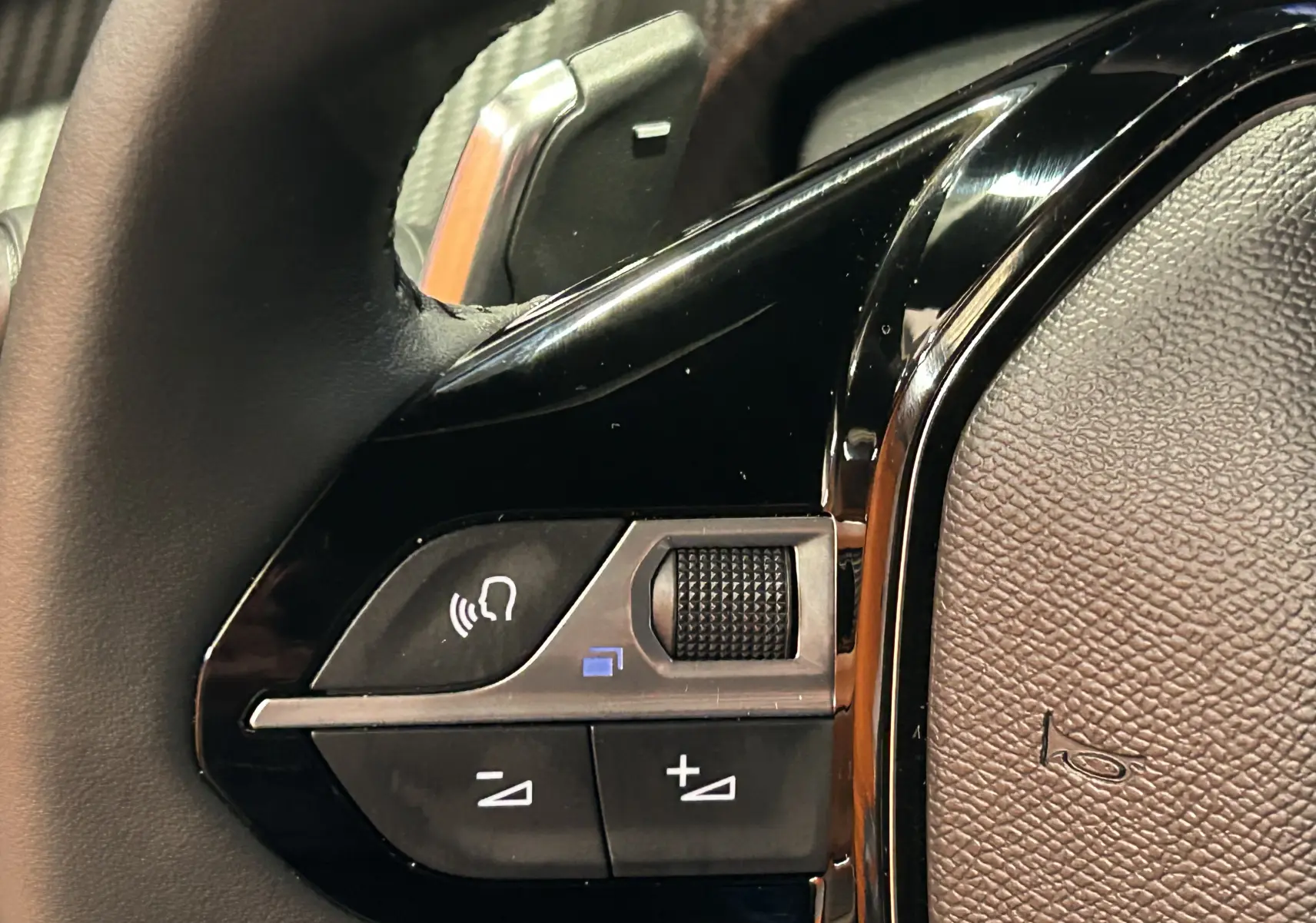 Gros plan sur les commandes vocales et volume au volant noir du Peugeot 2008 II Ph.2 Allure Hybrid 145 bleu Obsession.