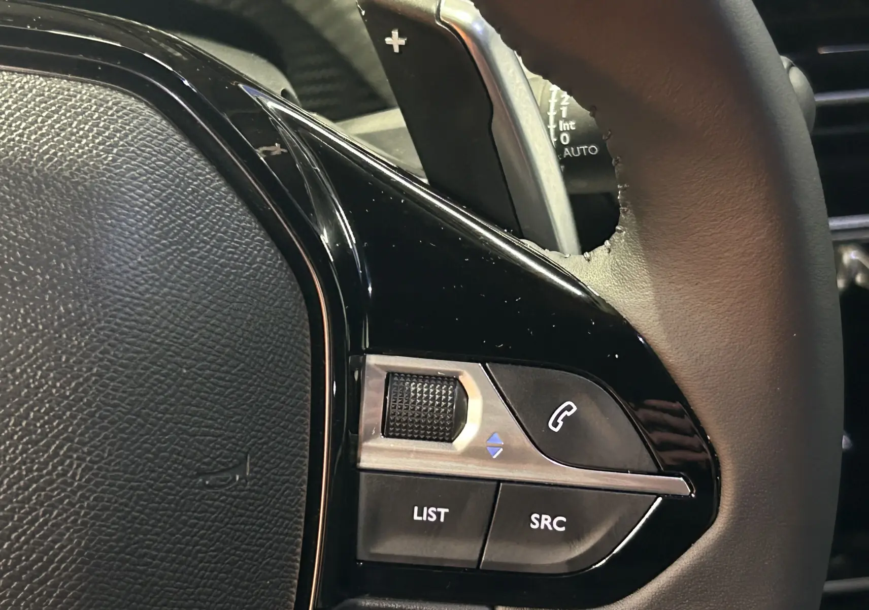 Gros plan sur les commandes du volant noir du Peugeot 2008 II Ph.2 Allure Hybrid 145, avec molette et boutons.