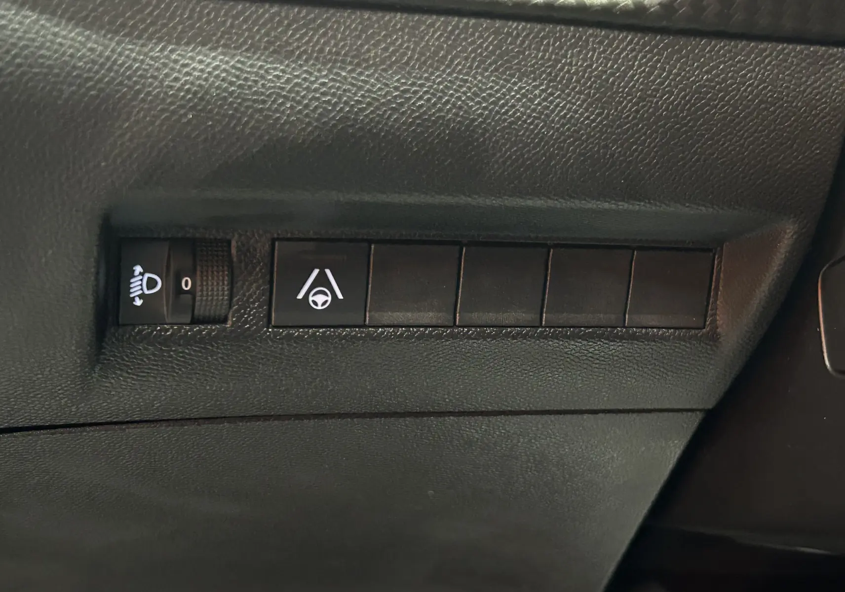 Gros plan sur les commandes d'assistance à la conduite et réglage des phares dans l'habitacle du Peugeot 2008 Bleu Obsession.
