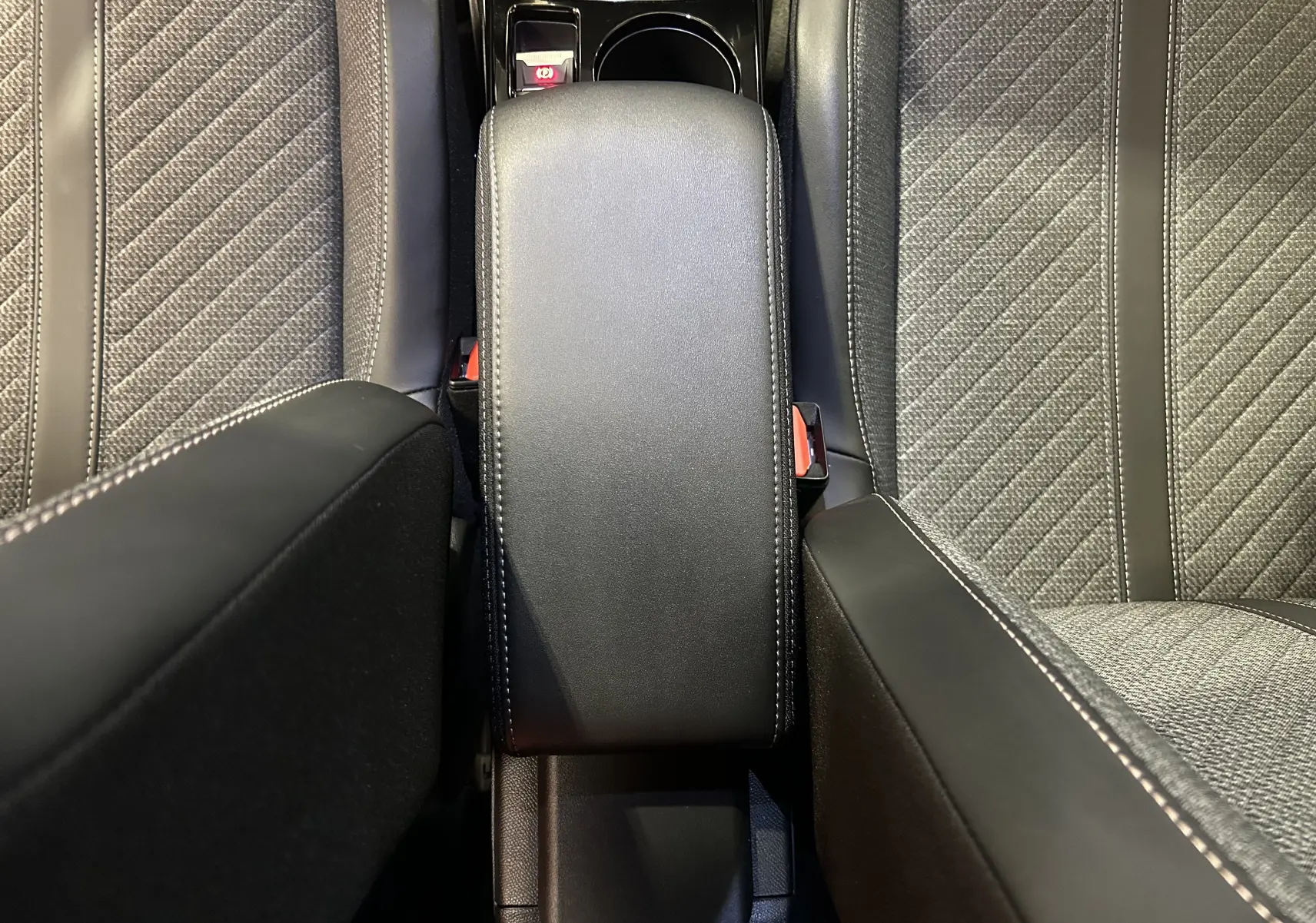 Vue plongeante sur l'accoudoir central en cuir noir et les sièges tissu gris du Peugeot 2008 II Ph.2 Allure Hybrid 2025.