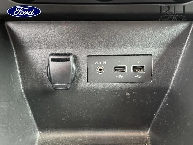 Vue rapprochée des prises auxiliaire et USB noires sur le tableau de bord d'une Renault Clio blanche.