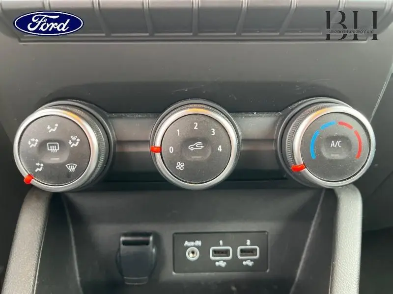 Panneau de commande de climatisation avec trois molettes noires dans un Renault Clio blanc, vue frontale rapprochée.
