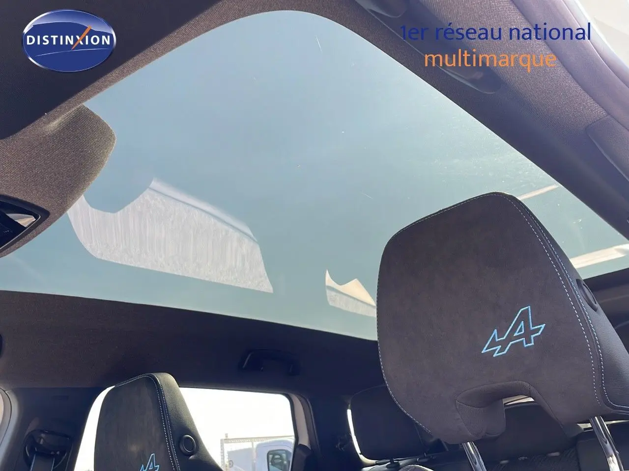 Détail du ciel de toit panoramique et appuie-tête noir avec logo Alpine bleu dans un Renault Espace blanc nacré.