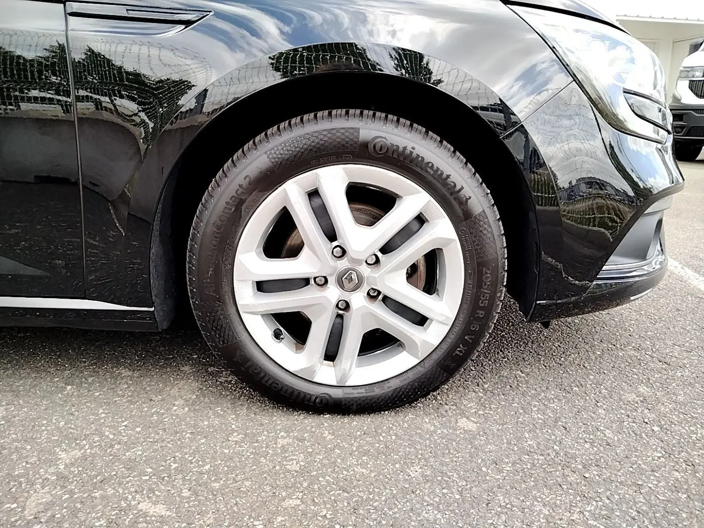 Gros plan sur la roue avant gauche d'une Renault Mégane IV Business noire, soulignant la jante argentée et le logo Renault central.