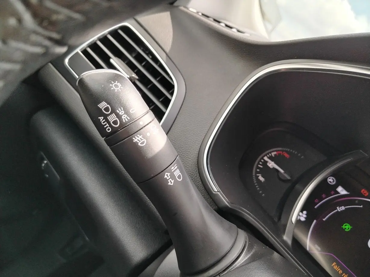 Gros plan sur la commande des phares et clignotants à gauche du volant dans l'habitacle noir d'une Renault Mégane IV Business.