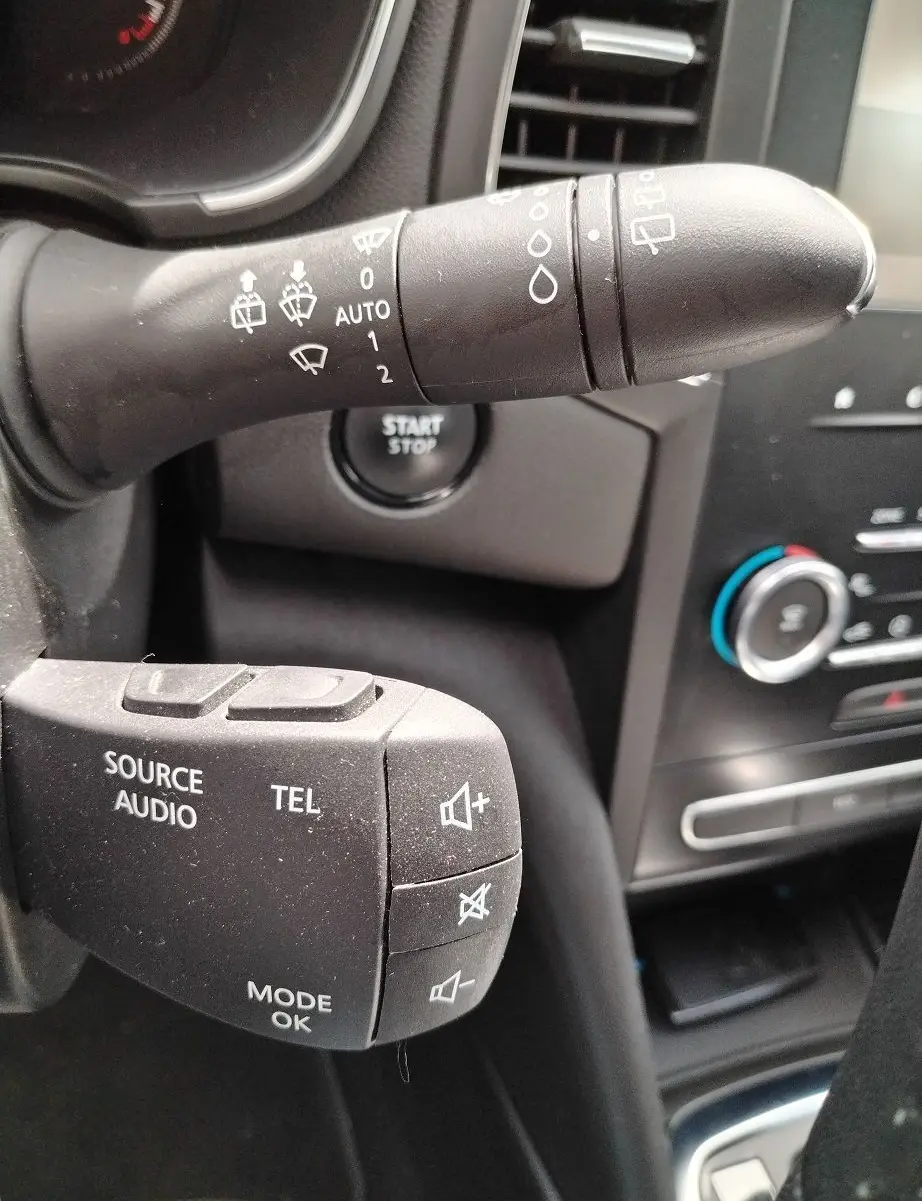 Gros plan sur les commandes au volant gauche de la Renault Mégane IV Business noire, montrant les boutons audio et essuie-glace.