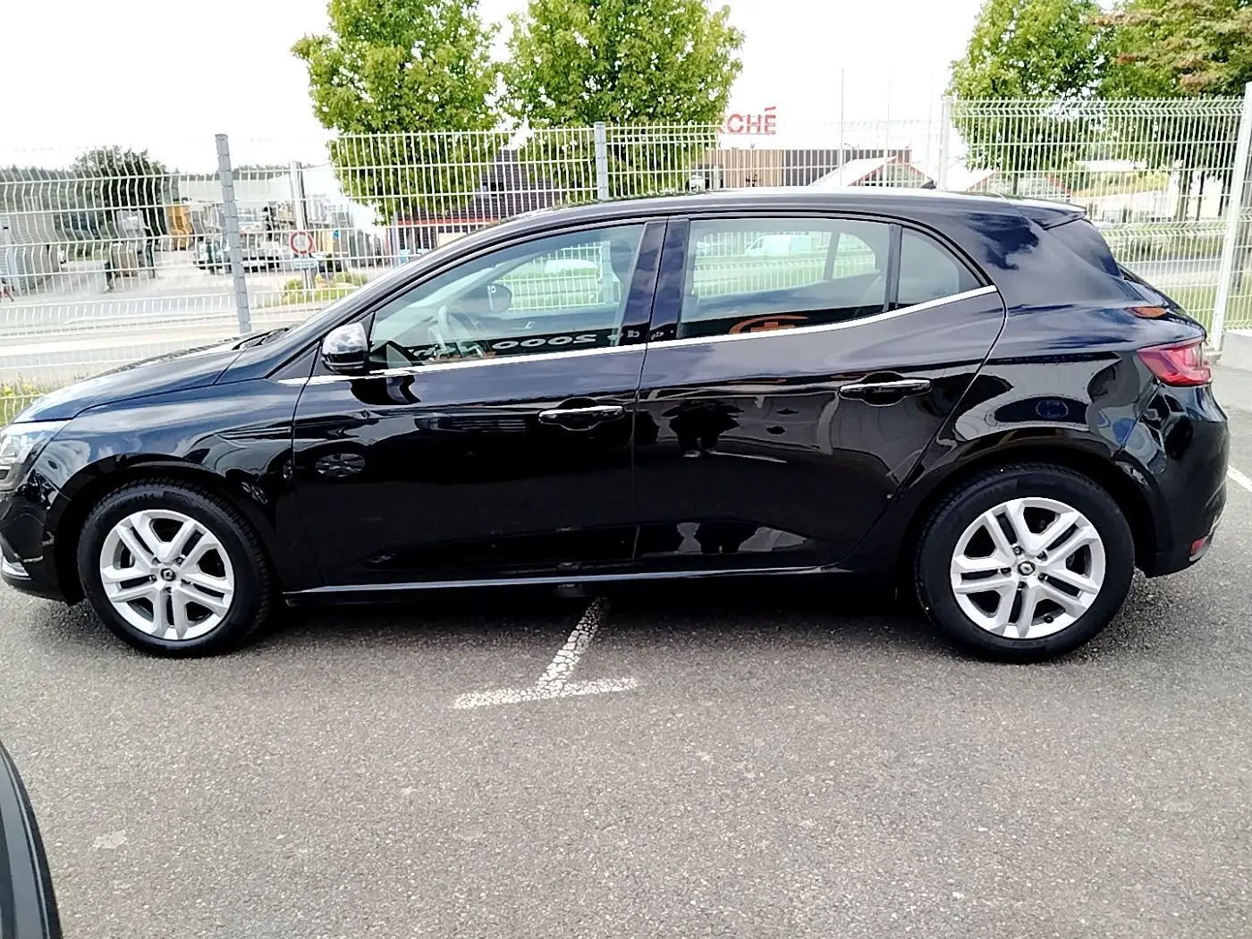 Profil côté gauche d'une Renault Mégane IV Business noire, garée sur un parking extérieur, roues alliage visibles.