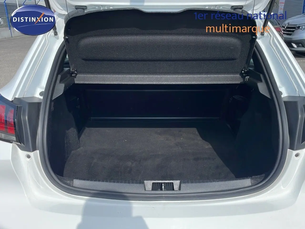 Coffre ouvert d'une Peugeot 208 blanc banquise vue arrière, montrant l'espace de chargement vide et propre.
