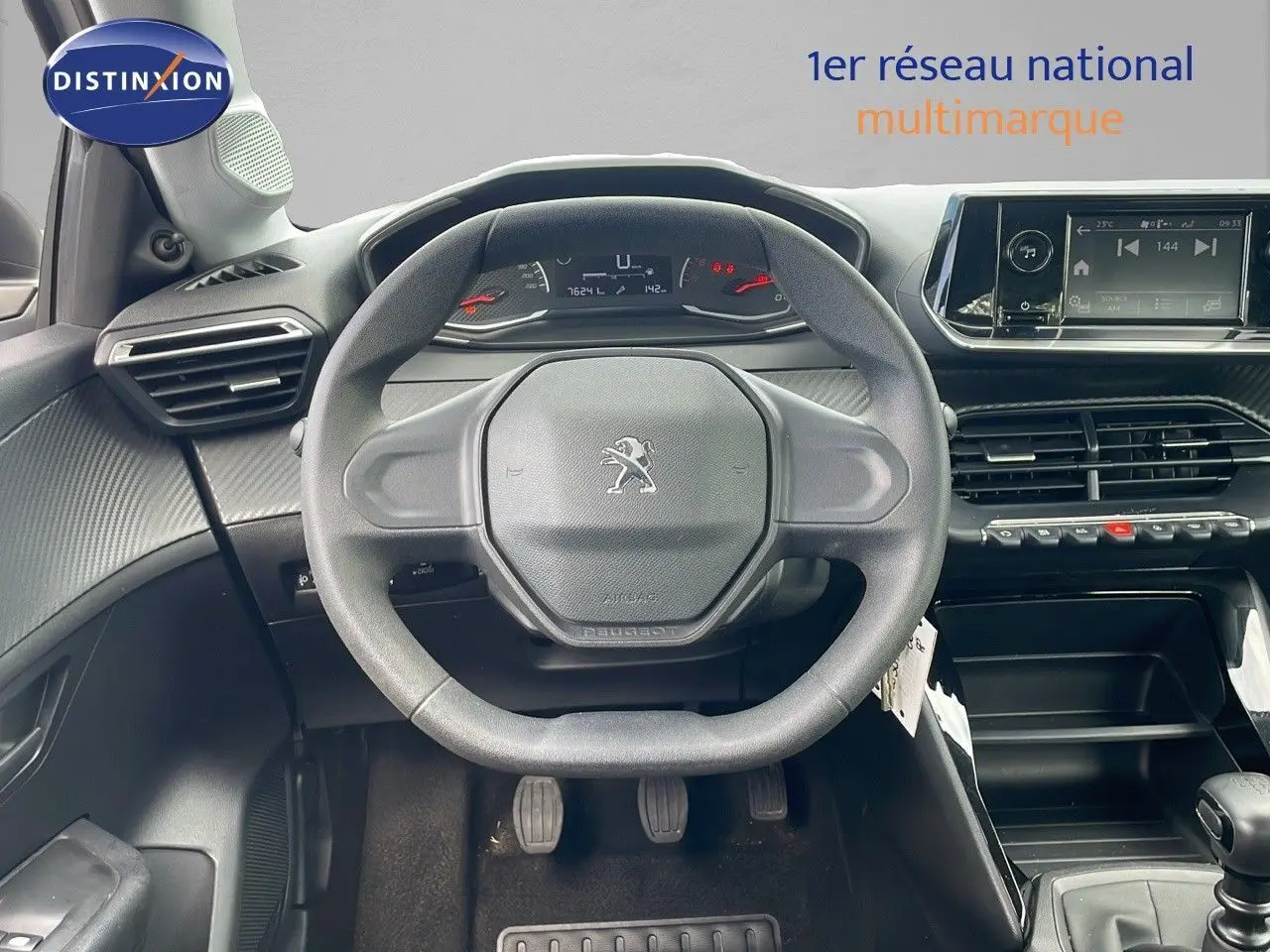 Vue frontale du poste de conduite de la Peugeot 208 blanche, volant compact et tableau de bord numérique visible.