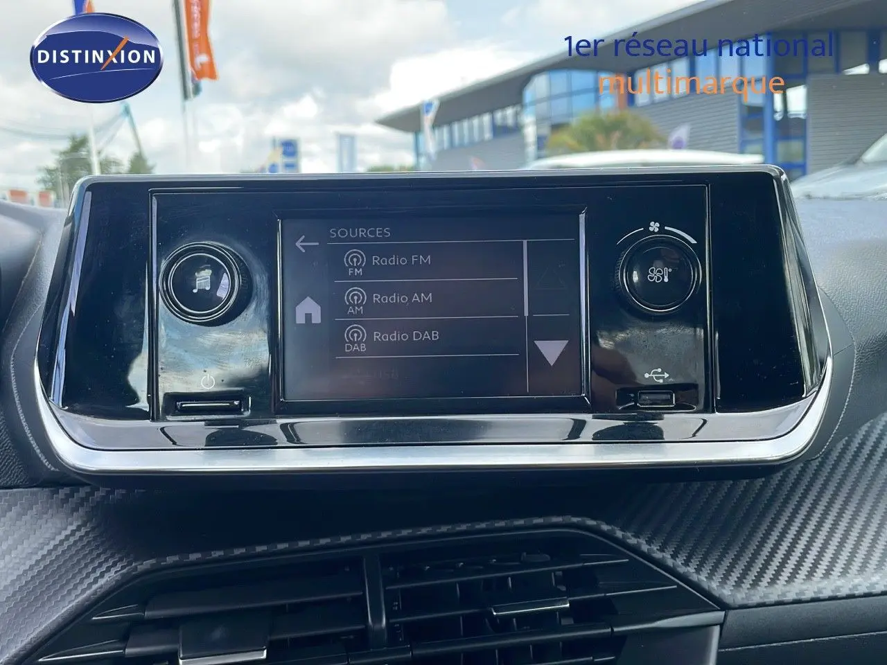 Écran tactile central du tableau de bord de la Peugeot 208 blanche, avec commandes audio et climatisation visibles.