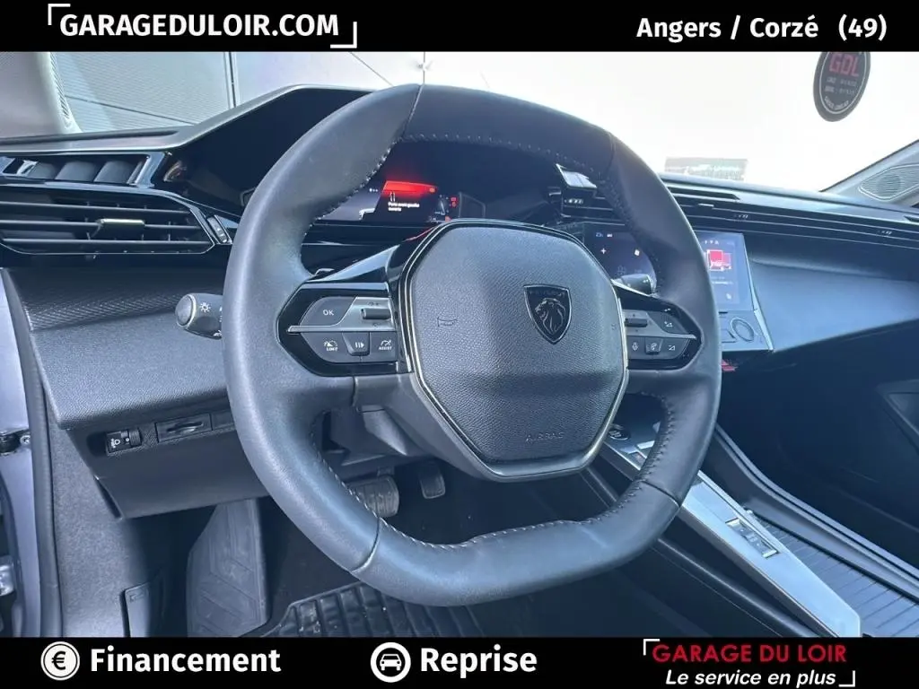 Vue intérieure centrée sur le volant cuir noir de la Peugeot 308 gris clair, avec tableau de bord digital et console tactile.