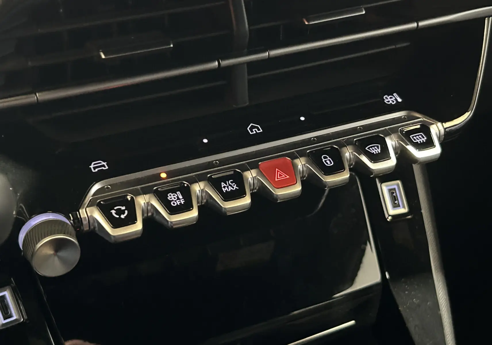 Gros plan sur la rangée de boutons de commande du tableau de bord du Peugeot 2008 gris, avec bouton rouge d’alerte au centre.