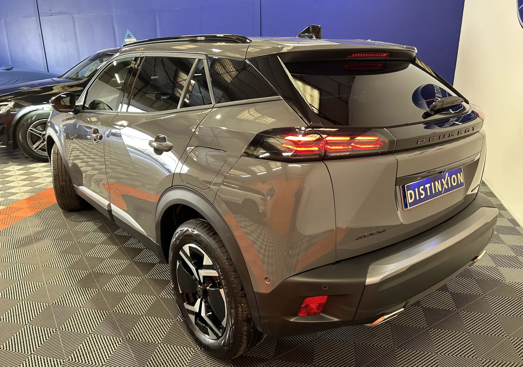Vue 3/4 arrière droite d’un Peugeot 2008 gris Selenium avec feux arrière allumés dans un showroom.