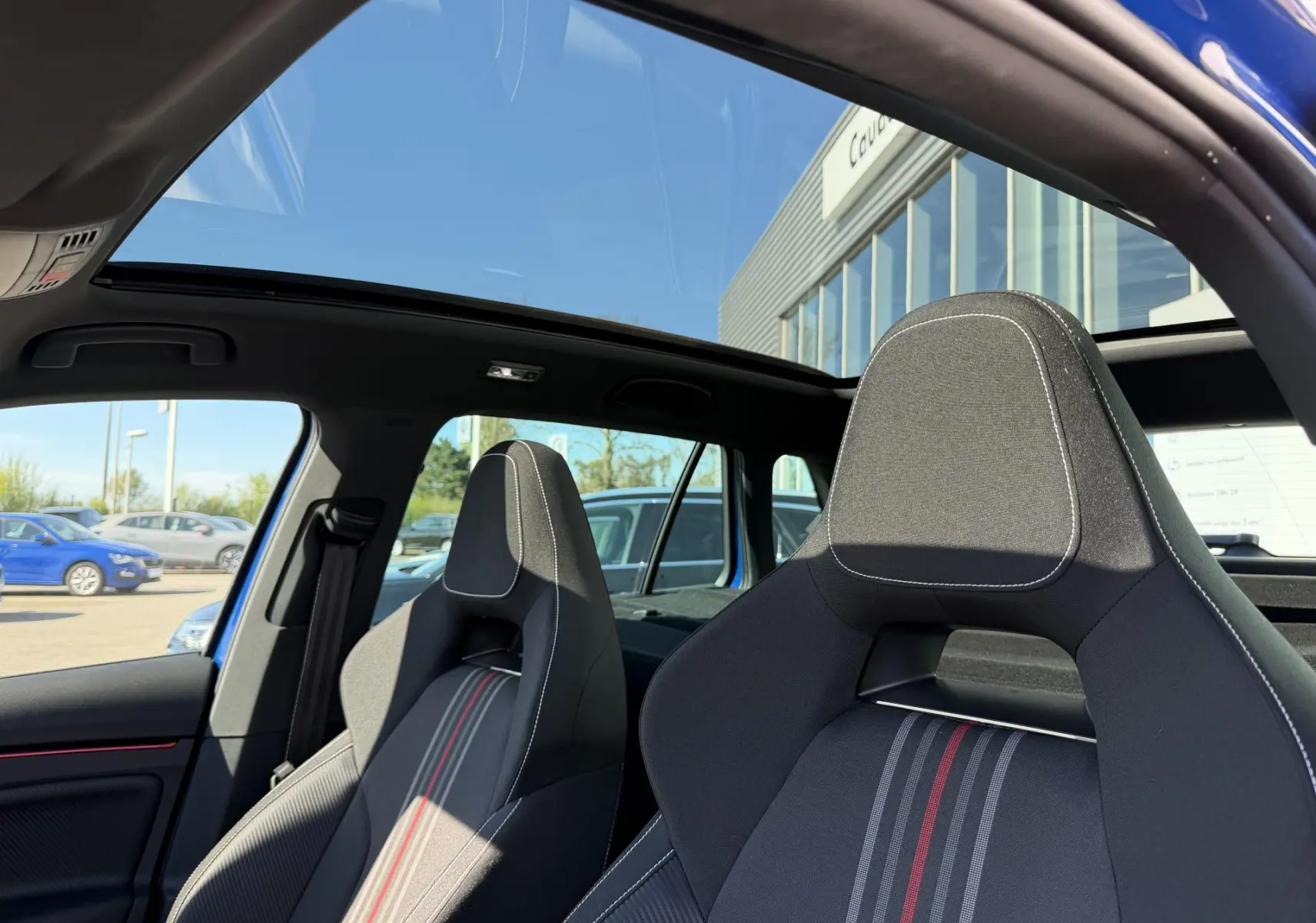Vue intérieure sur les sièges sport avant gris avec surpiqûres blanches et toit panoramique du Skoda Kamiq bleu 2025.