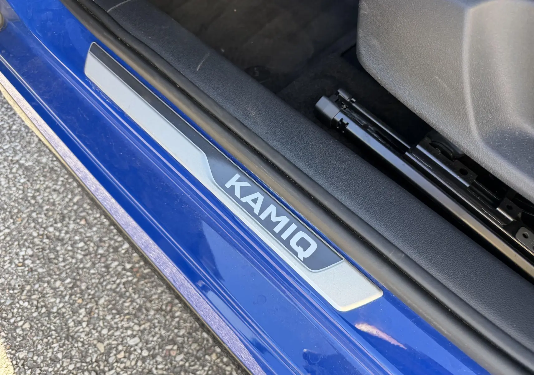 Gros plan sur la plaque de seuil de porte "KAMIQ" sur le côté gauche d'une Skoda Kamiq bleue.