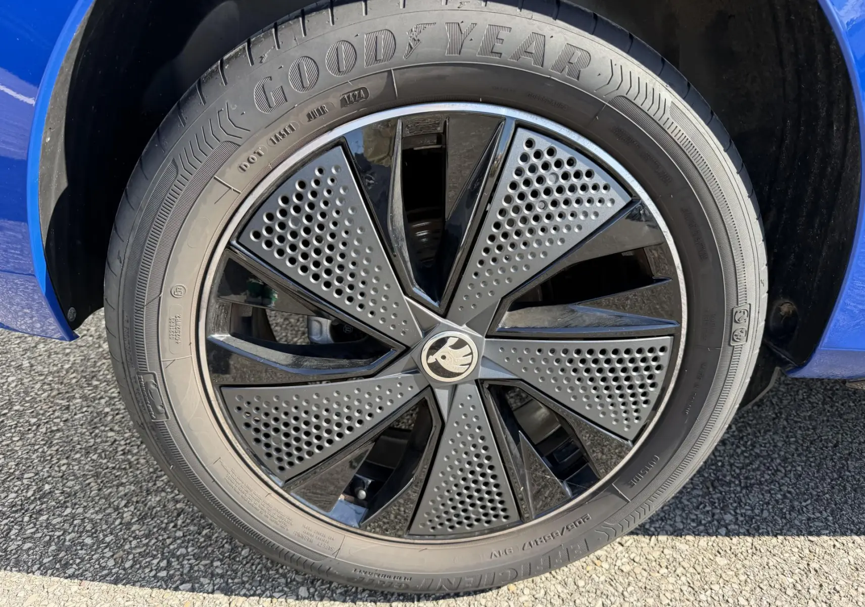 Gros plan sur la jante alliage noire 17 pouces du Skoda Kamiq bleu, avec pneu Goodyear visible sur fond de bitume.