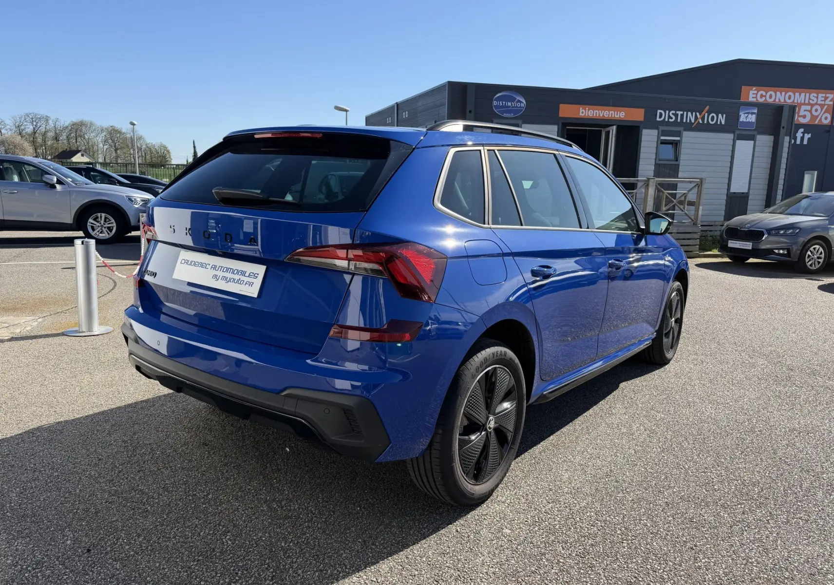 Vue 3/4 arrière droite d'un Skoda Kamiq bleu avec jantes alliage noires sur un parking extérieur.