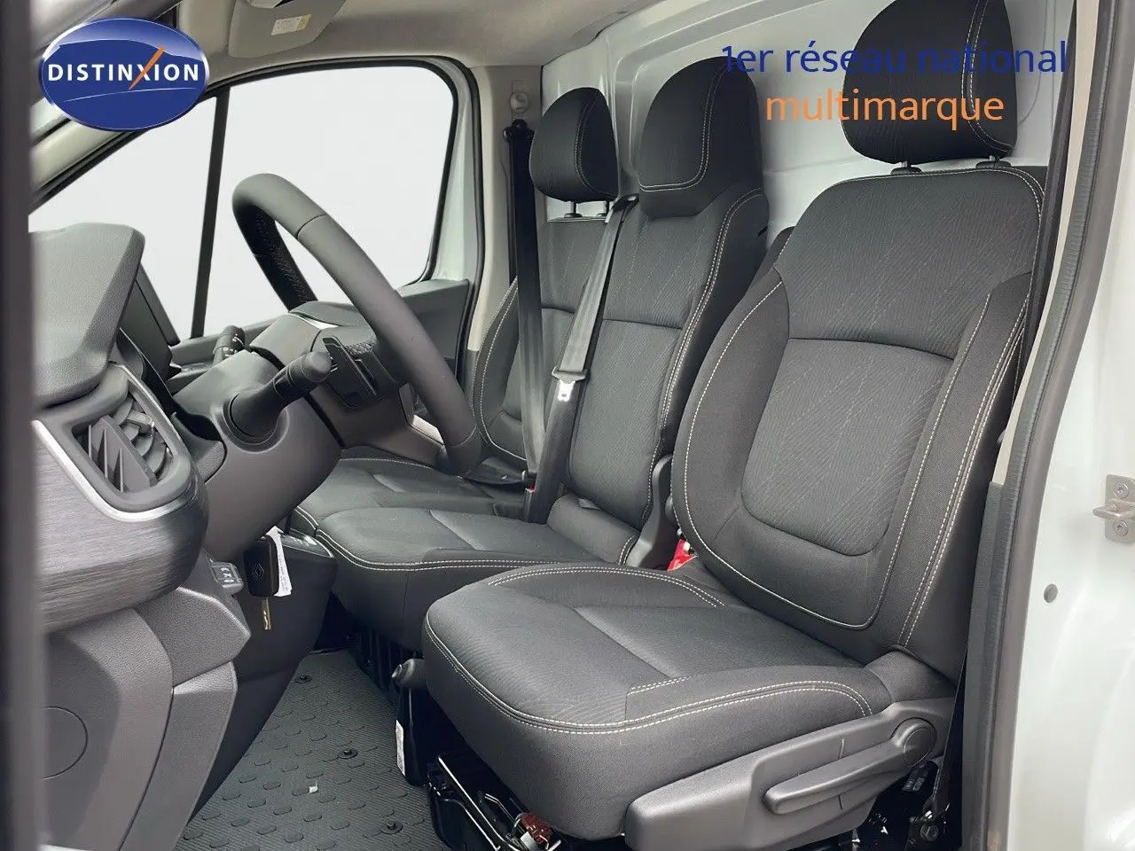 Vue intérieure côté conducteur du Renault Trafic Fourgon blanc glacier 2025, sièges noirs avec surpiqûres claires et volant visible.