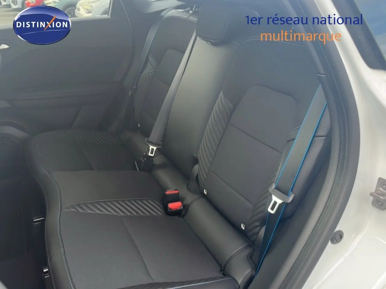 Vue intérieure côté droit montrant les sièges arrière noirs avec surpiqûres et ceinture de sécurité bleue d'une Renault Symbioz blanche nacrée.