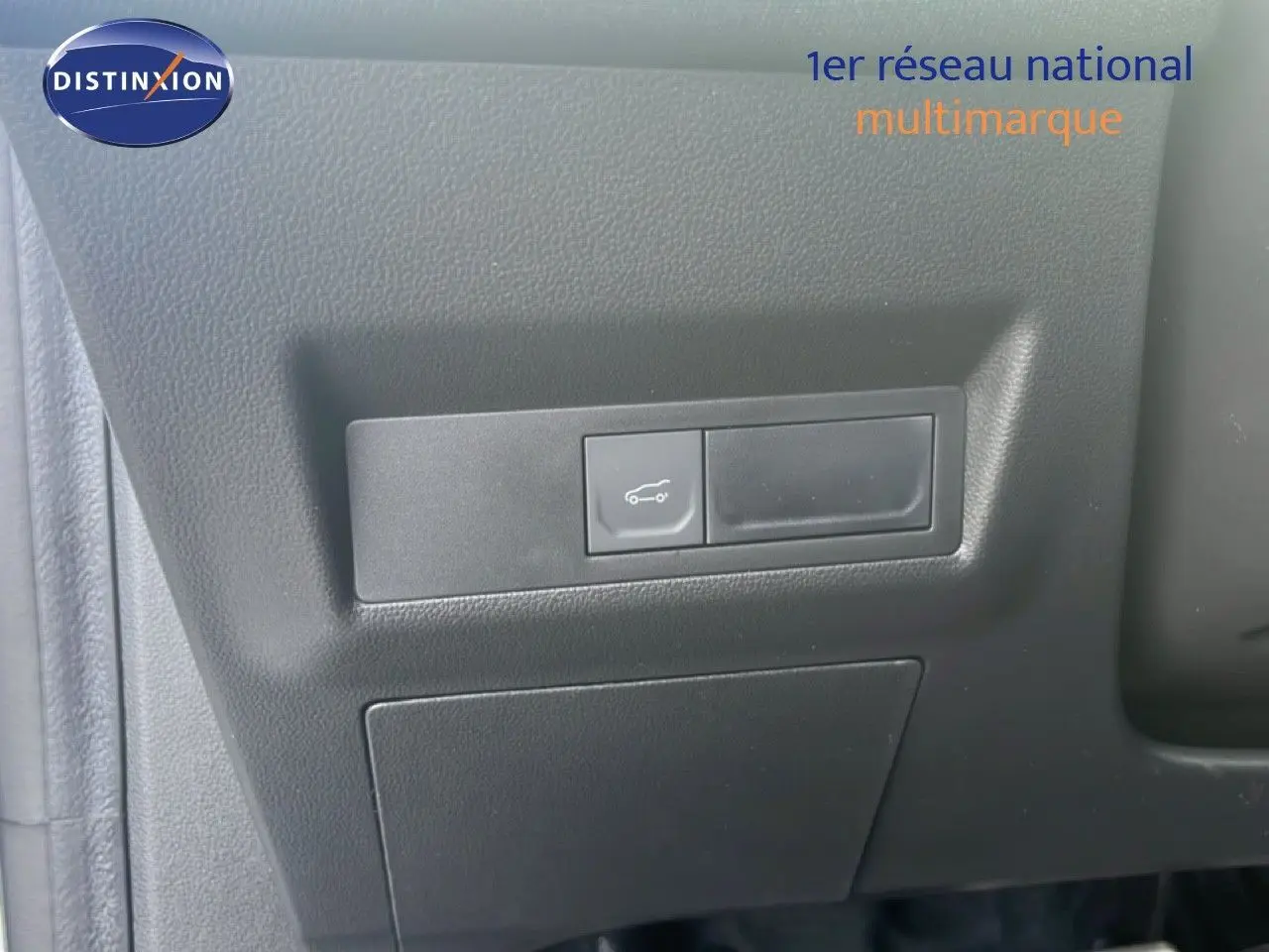 Bouton d'ouverture du coffre sur panneau intérieur noir d'une Renault Symbioz blanche nacrée, vue rapprochée.