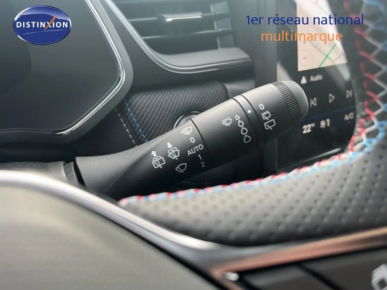 Gros plan sur la commande d’essuie-glace à gauche du volant perforé avec surpiqûres tricolores dans le Renault Symbioz blanc nacré.