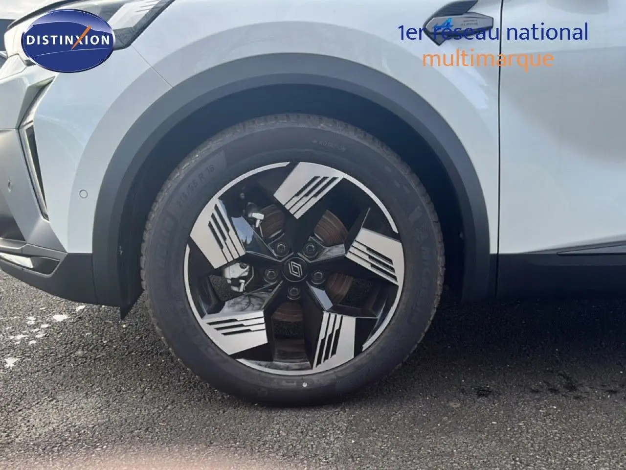 Gros plan sur la roue avant gauche d’un Renault Symbioz blanc nacré avec jante au design noir et argent.