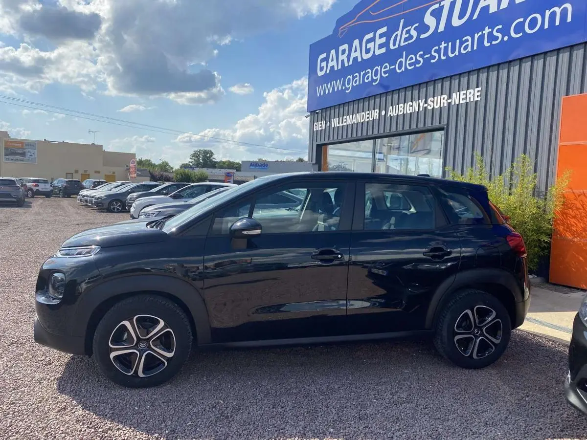 Profil côté gauche d'un Citroën C3 Aircross noir 2021, version Shine, stationné devant un garage avec jantes distinctives.