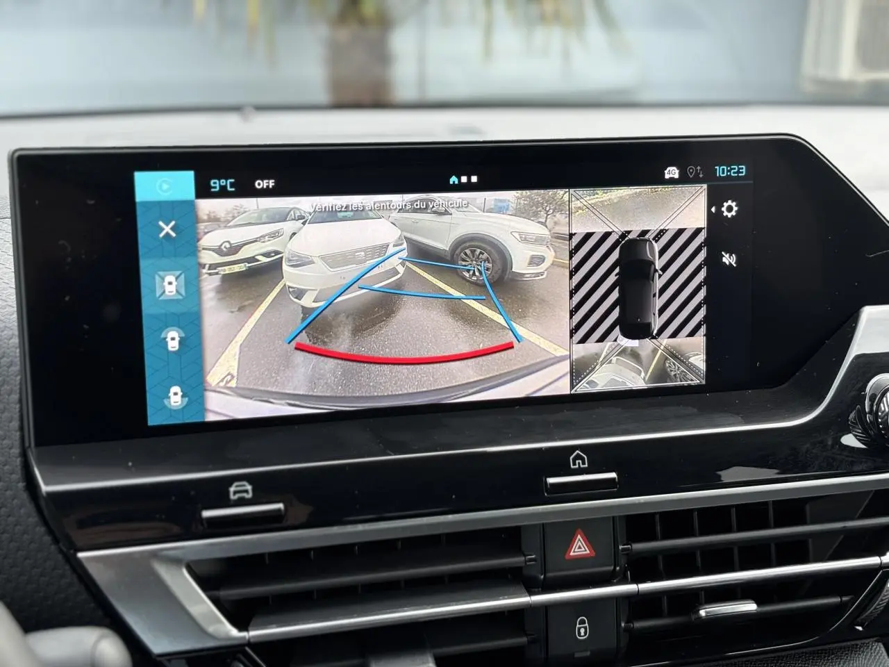 Écran tactile intérieur montrant la caméra 360° avec vue arrière sur une voiture blanche en stationnement.