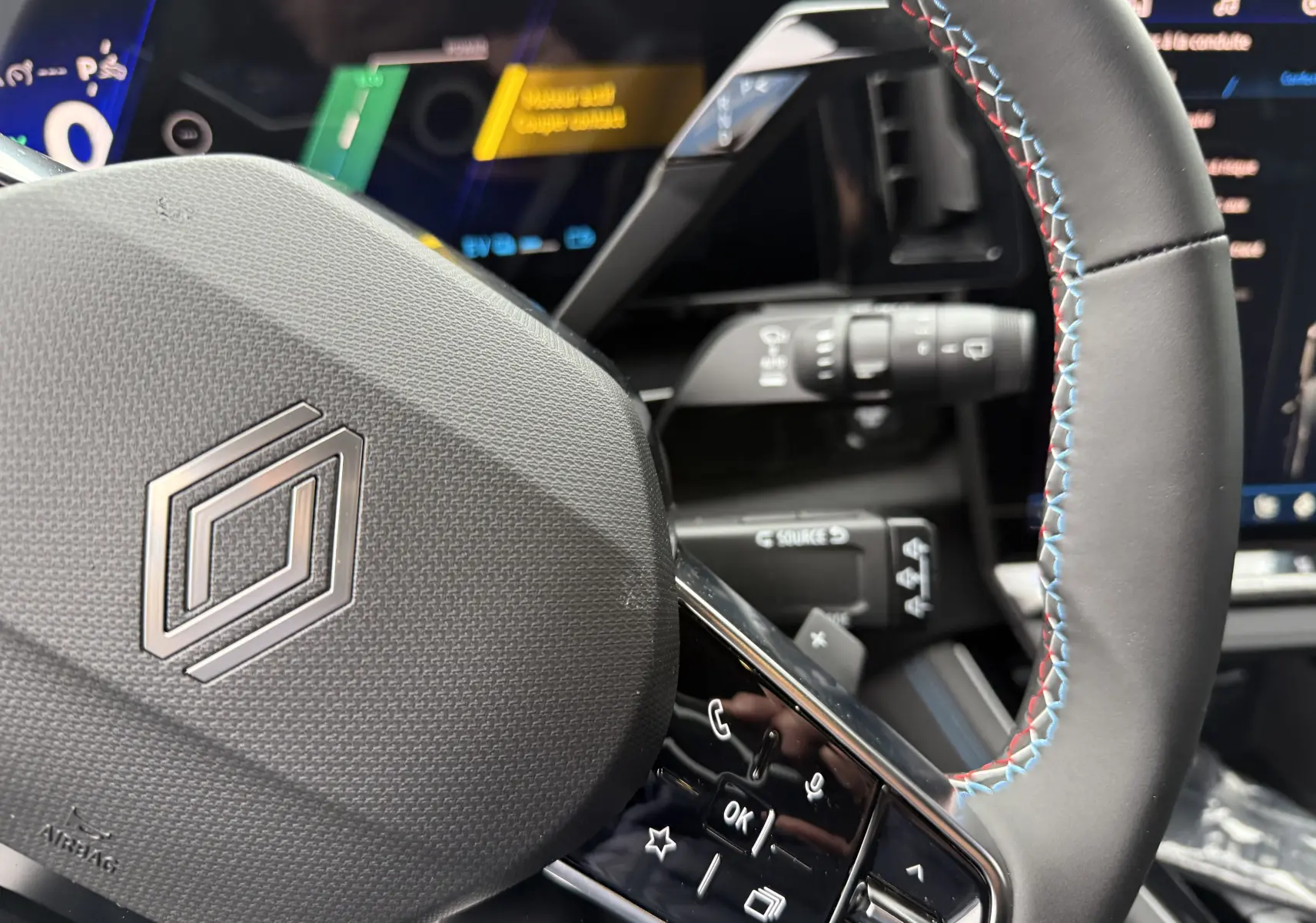 Gros plan sur le volant noir avec surpiqûres tricolores du Renault Austral 2025, tableau de bord digital en arrière-plan.