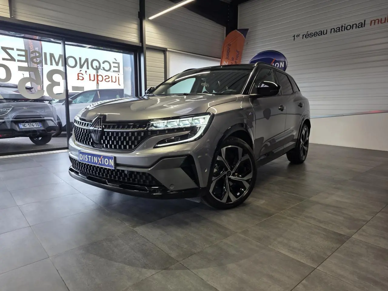 Renault Austral gris foncé en 3/4 avant droit, avec calandre à damier et jantes alliage noires diamantées.