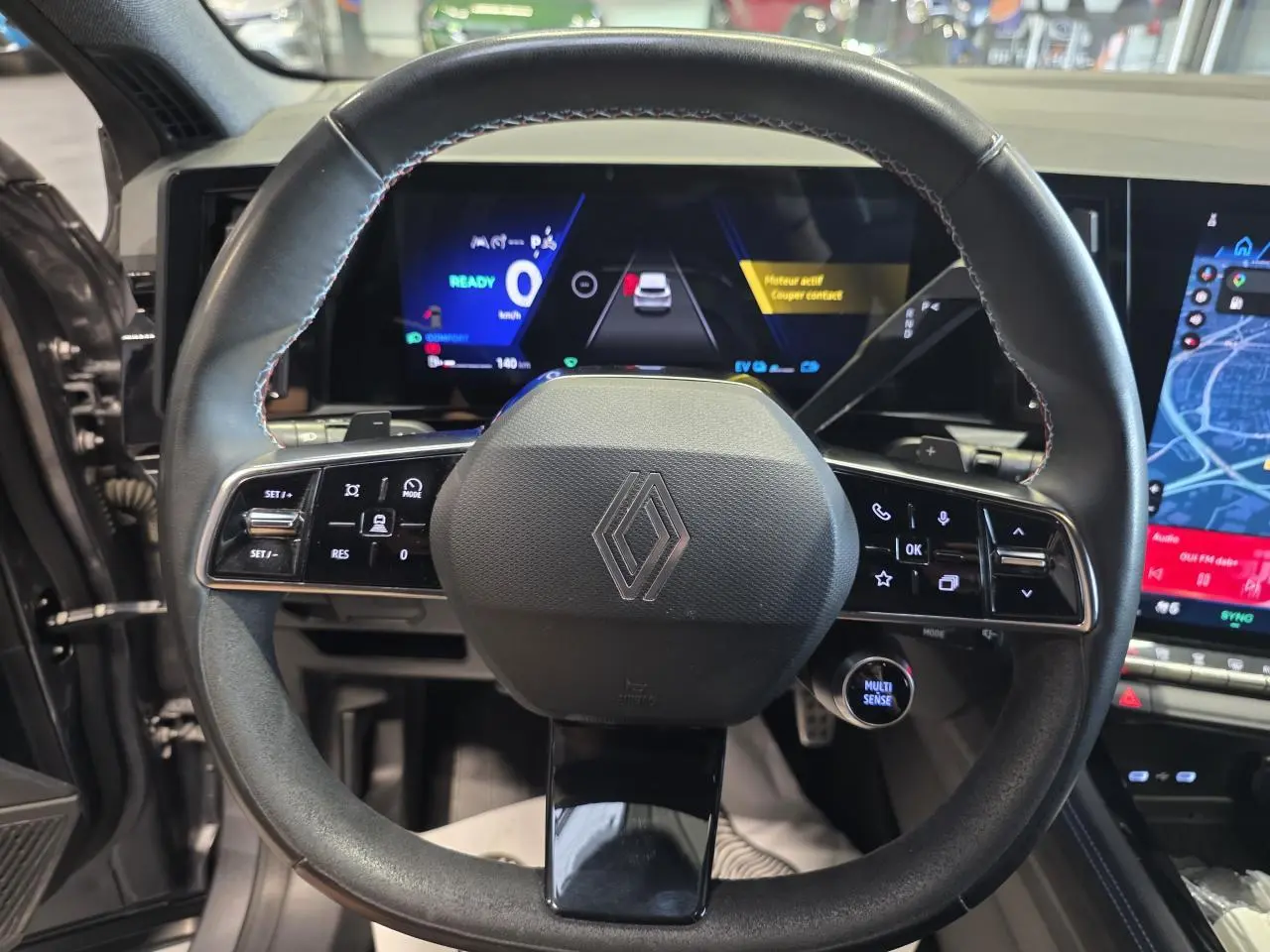 Vue rapprochée du volant Alcantara noir avec surpiqûres bleues du Renault Austral 2024, tableau de bord numérique en arrière-plan.
