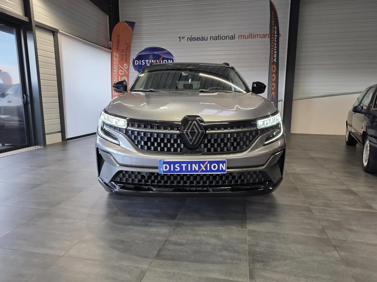Vue frontale d’un Renault Austral gris foncé avec calandre damier ice black et feux LED allumés en showroom.