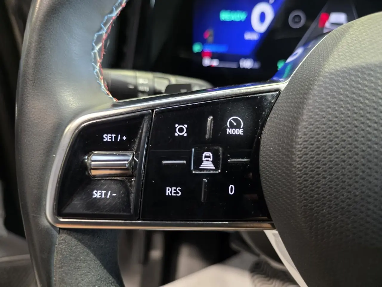 Gros plan sur les commandes du volant à gauche du Renault Austral gris foncé, avec insert Alcantara et surpiqûres bleues.