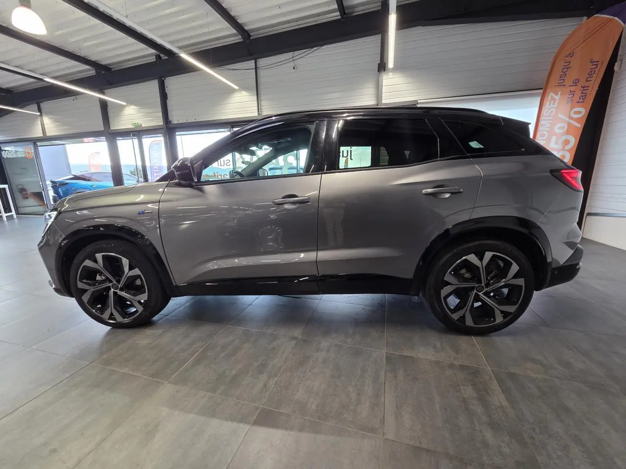 Vue de profil côté gauche d'un Renault Austral gris foncé avec jantes alliage 20 pouces en intérieur showroom.