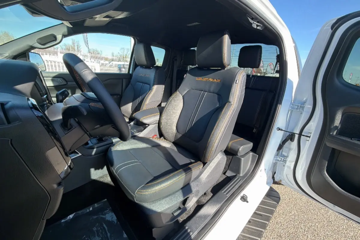 Vue intérieure côté conducteur du Ford Ranger blanc pur 2025, sièges noirs avec surpiqûres orange Wildtrak visibles.