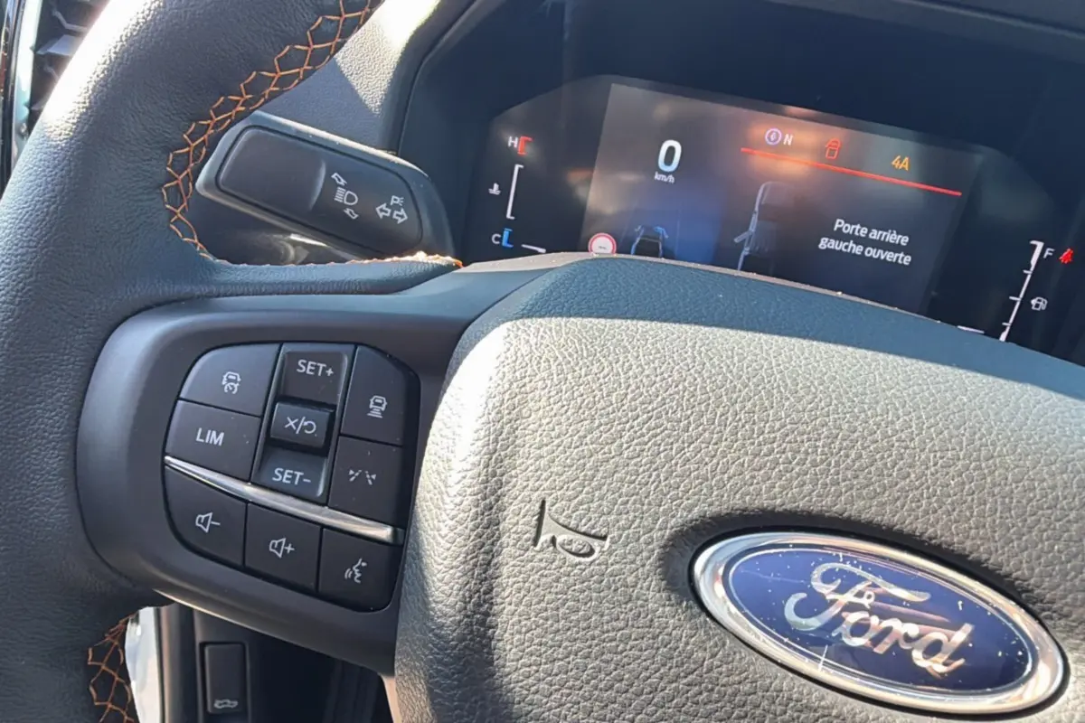 Gros plan sur le volant cuir noir avec surpiqûres orange et tableau de bord digital du Ford Ranger blanc 2025.