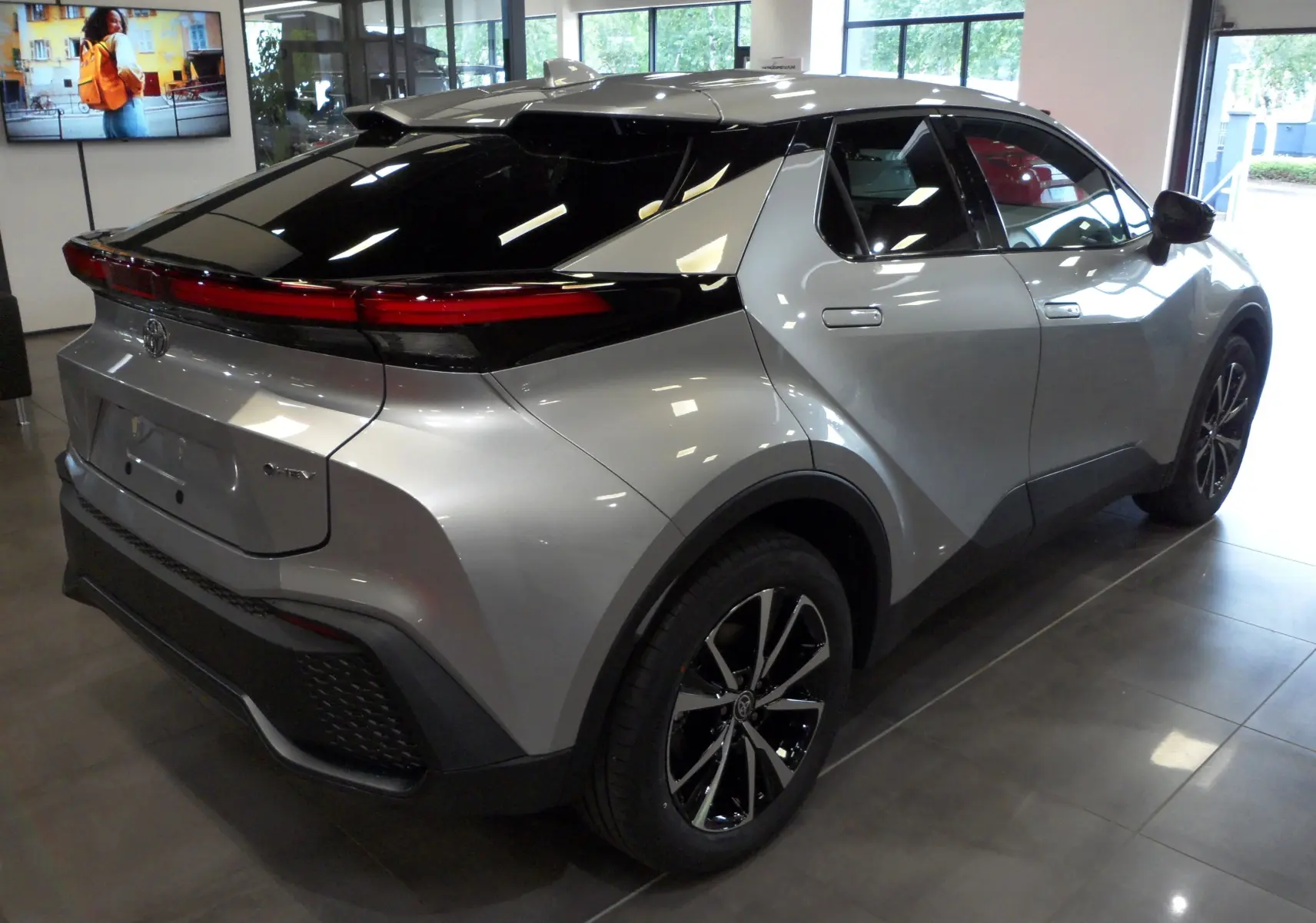 Vue 3/4 arrière droite du Toyota C-HR hybride gris minéral avec toit noir brillant et jantes bi-ton en showroom.