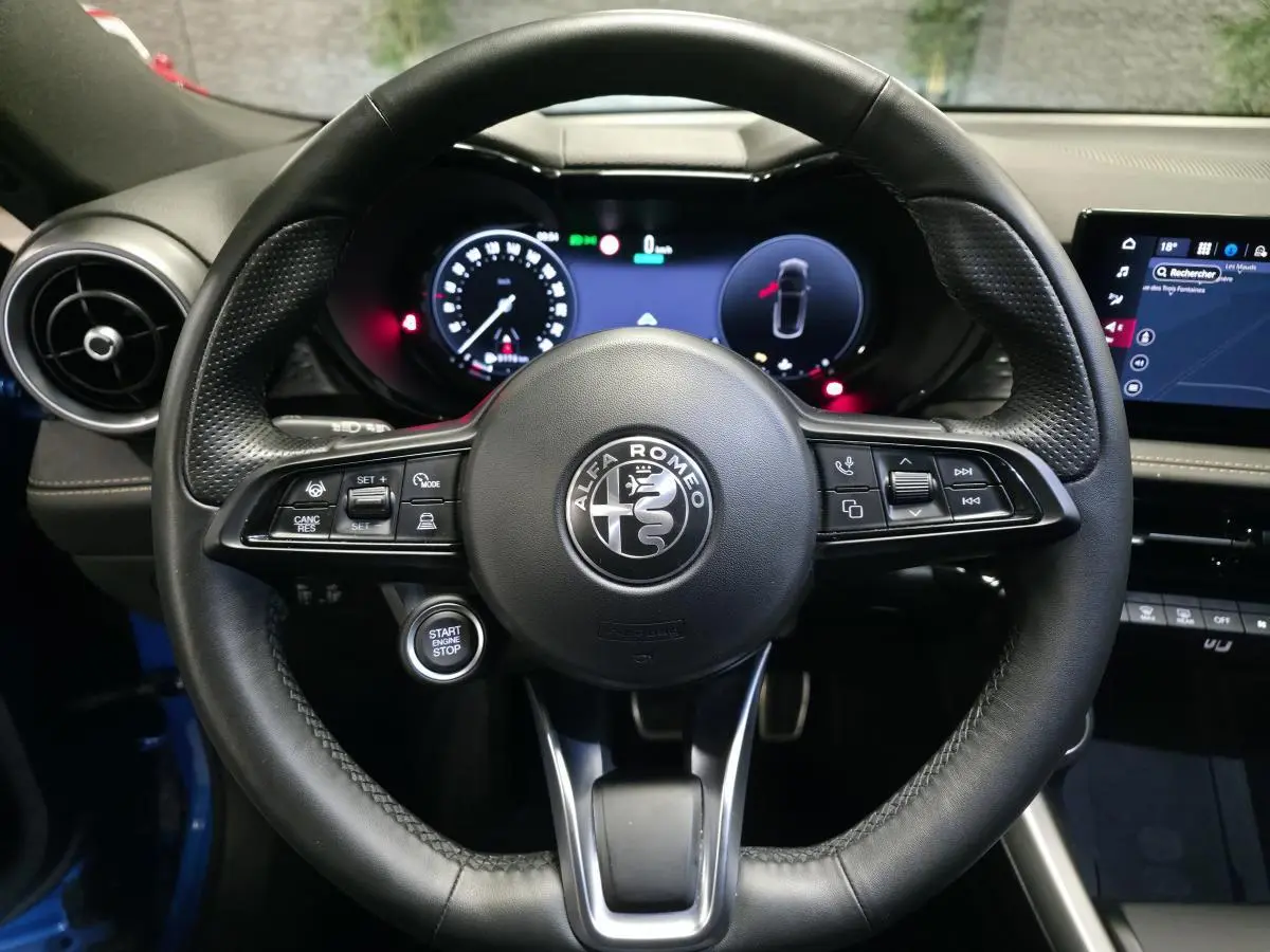Vue frontale du volant en cuir noir de l'Alfa Romeo Tonale 2025, avec tableau de bord digital et bouton start/stop visible.