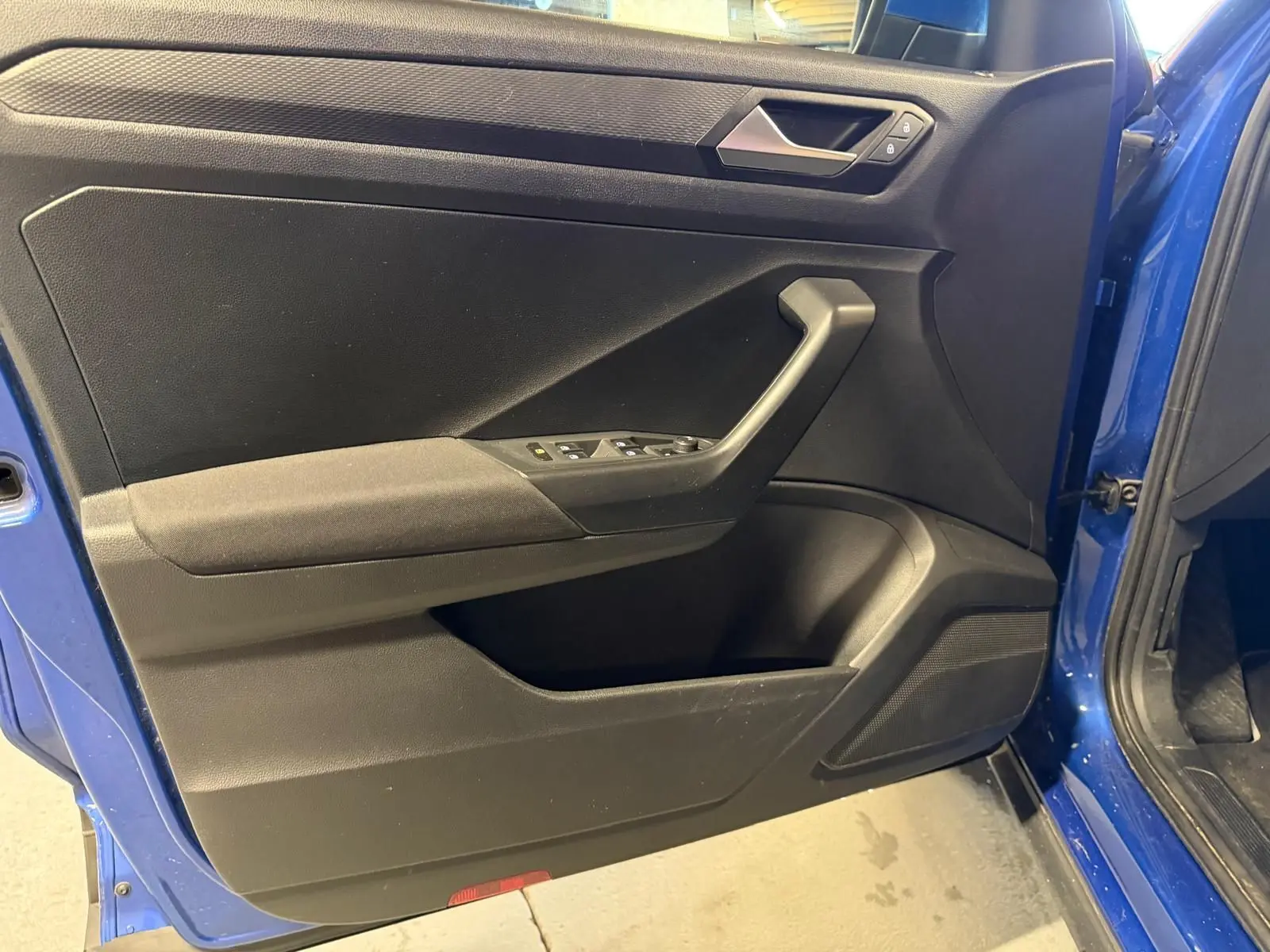 Vue intérieure de la porte avant gauche bleu vif du Volkswagen T-Roc avec commandes de vitres et poignée noire.
