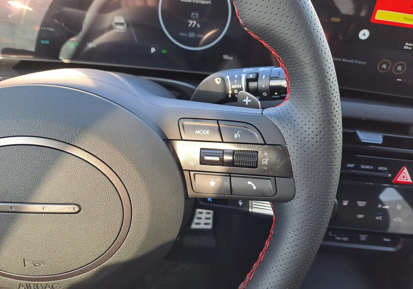 Gros plan sur le volant perforé noir avec surpiqûres rouges du Hyundai Tucson 2025, montrant les commandes multimédia et tableau de bord digital.