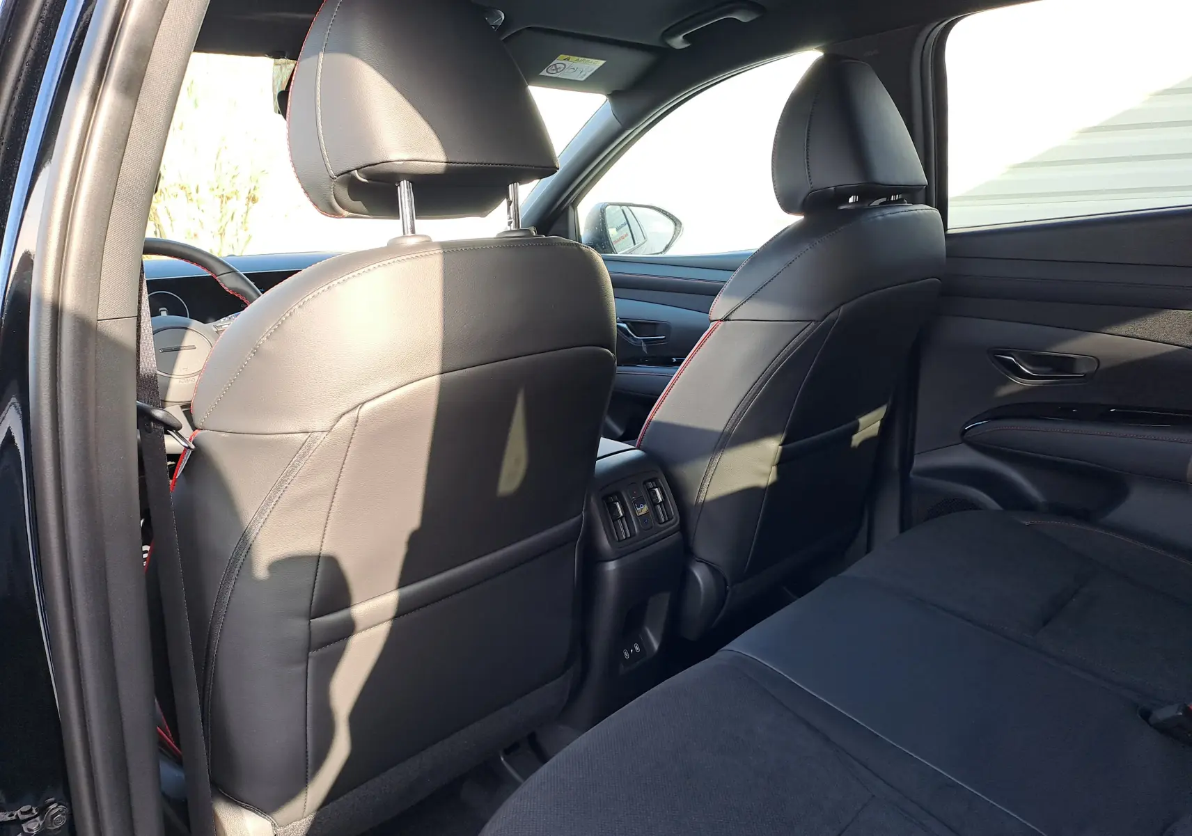 Vue intérieure arrière du Hyundai Tucson 2025 noir abyss, montrant les sièges avant en cuir noir avec surpiqûres rouges.