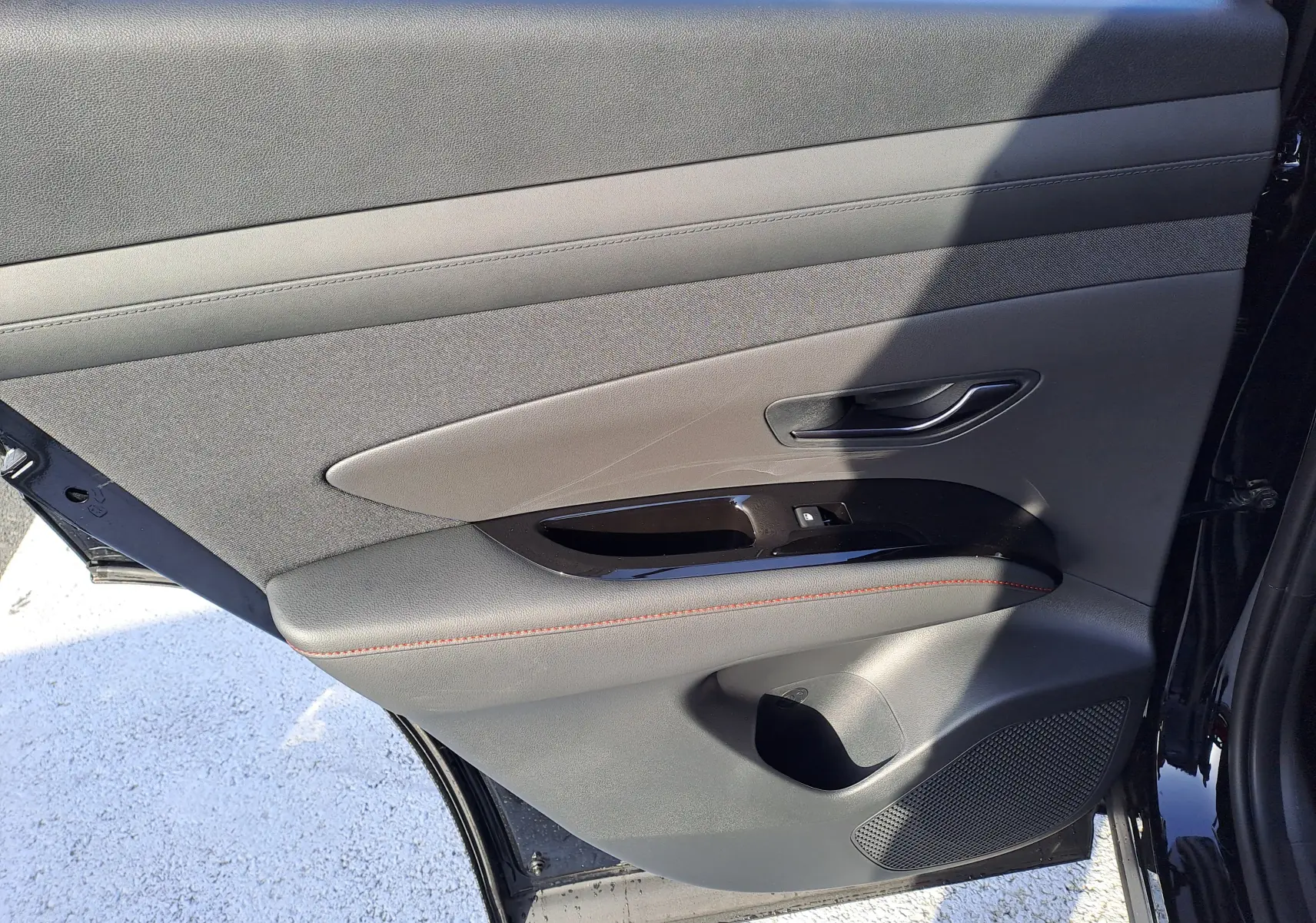 Vue intérieure de la porte arrière droite du Hyundai Tucson 2025 en Abyss Black, avec garniture grise et surpiqûres rouges.