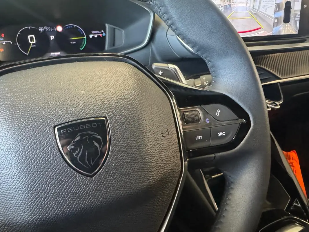 Gros plan sur le volant cuir noir du Peugeot 2008 Hybrid 145 Allure 2025 avec commandes intégrées et tableau de bord numérique.